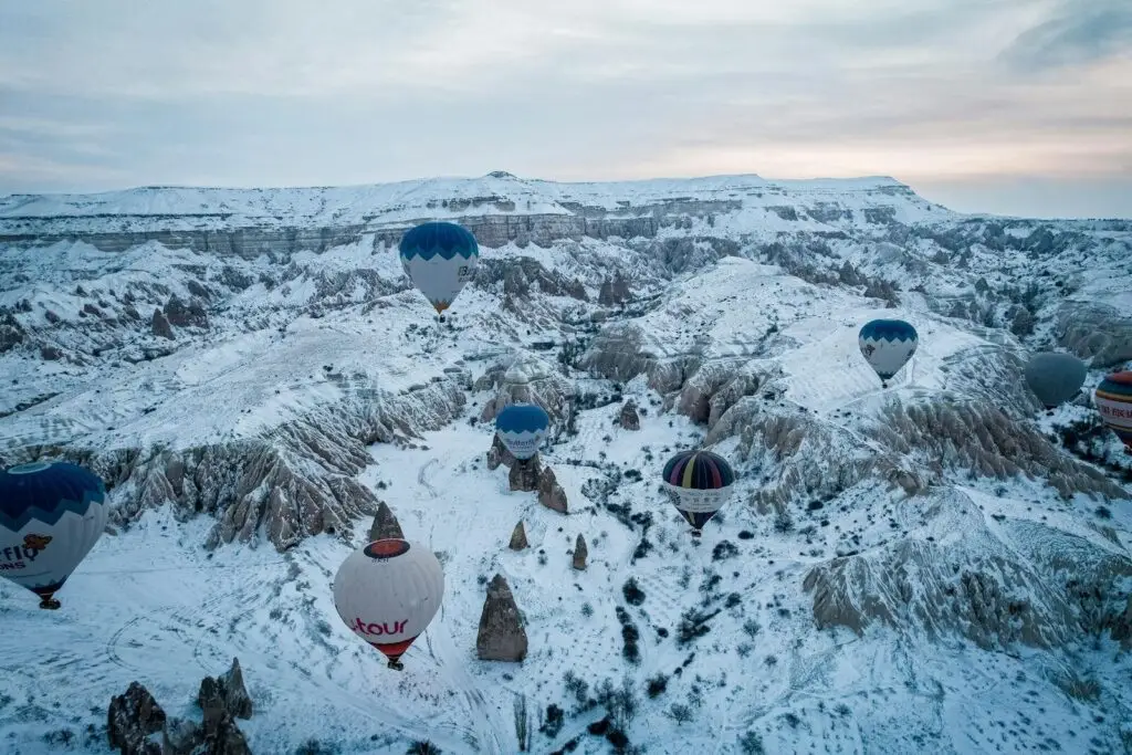 Beautiful aerial view of hot air balloons floating over snowy Cappadocia mountains during winter.