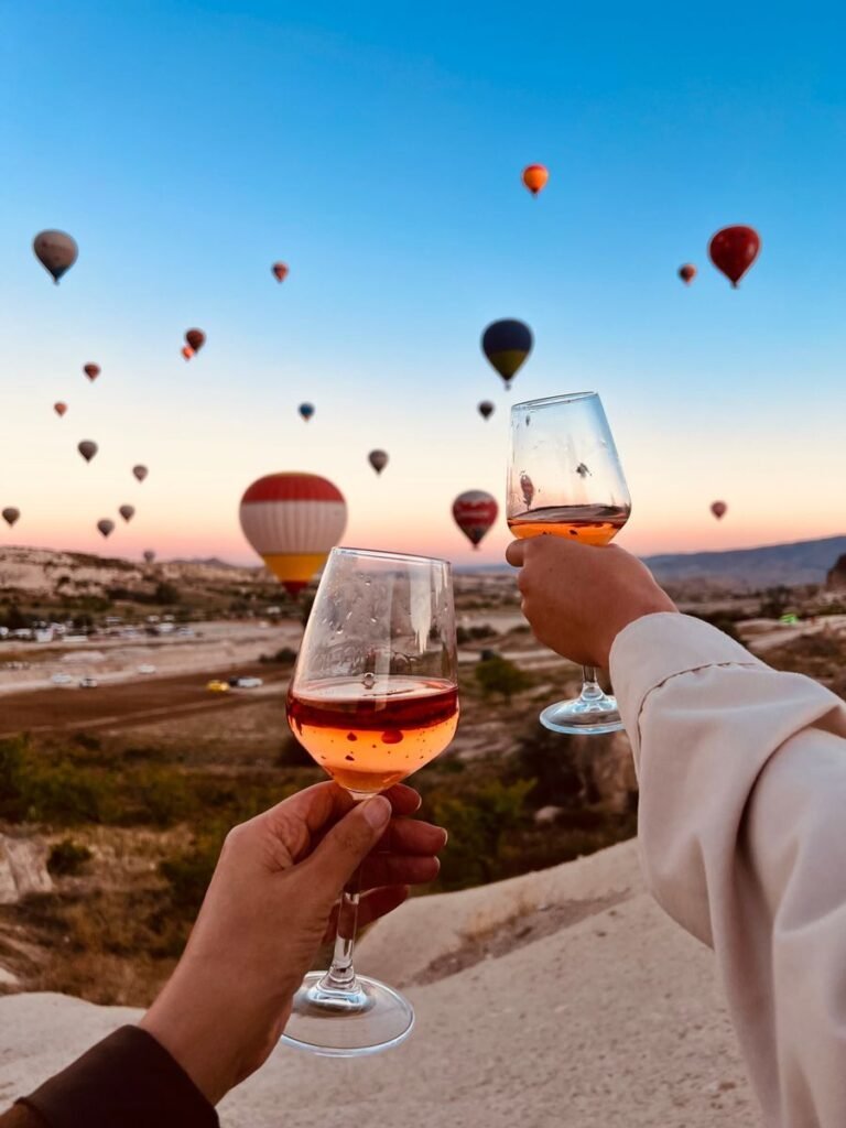 A scenic view of hot air balloons over Cappadocia with two glasses of rose wine.