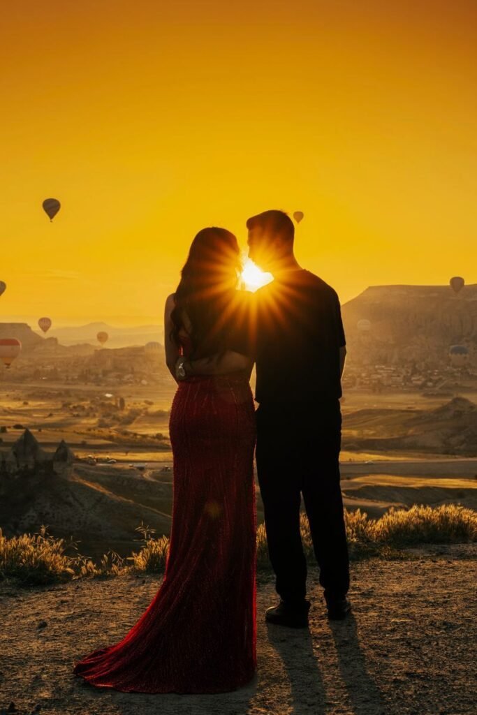 Couple standing at sunset with hot air balloons in the background, embracing love and adventure.